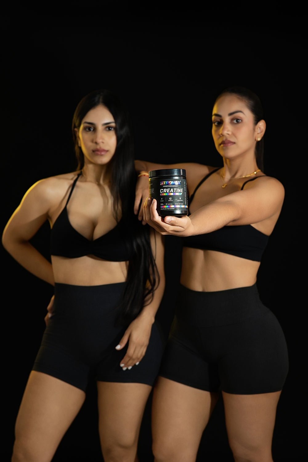 Dos mujeres con ropa deportiva presentan el pote de creatina STRONGA Performance